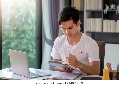 Young Asian Man Is Taking Notes On The Laptop Table At Home.