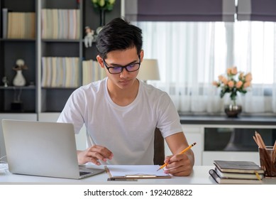 Young Asian Man Is Taking Notes On The Laptop Table At Home.