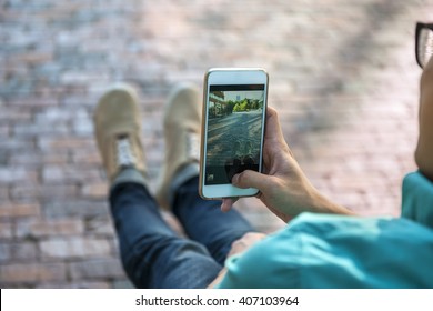 Young asian man taking photo of street and his feet with smartphone