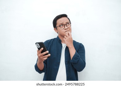 Young Asian man  thinking and concentrating while holding books and handphone. Asian student thinking and looking for ideas while holding phone over white background - Powered by Shutterstock