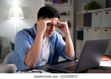 Young Asian man tired from hard work with eyes closed using both hands to massage temples and head to relieve exhaustion pain and anxiety. 
