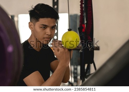 A young asian man training his punching reflexes and hand -eye coordination on a yellow double end bag. Boxing practice at the gym.