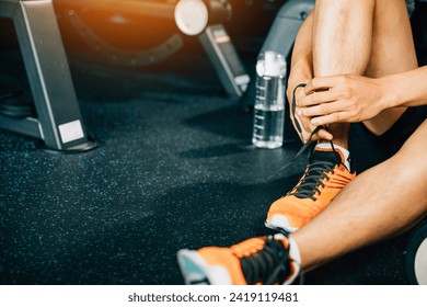 Young Asian man tying his shoelaces in his home gym before starting his workout routine. The shot showcases his sporty shoes and the water bottle he uses to stay hydrated during exercise - Powered by Shutterstock