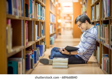 Young Asian Man University Student Reading Book Sitting By Bookshelf In College Library For Education Research And Self Improvement. Scholarship And Educational Opportunity. World Book Day Concept