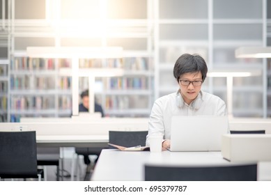 Young Asian Man University Student Working With Laptop Computer And Notebook In Library, Self Learning And College Lifestyle Concepts