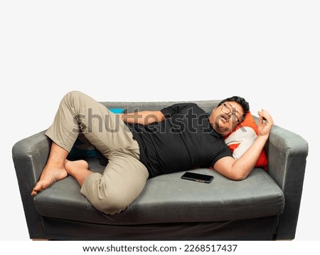 young asian man use eyeglasses and black t-shirt lay on the grey couch get sleep.asian lazy man with.boy enjoy the living room sofa and sleep mobile phone beside him white background fat guy sleeping