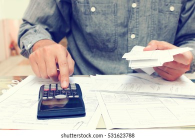 Young Asian Man Using Calculator And Calculating Bills In Home Office.