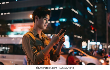 Young Asian Man Is Using His Phone While Walking In The Street At Night
