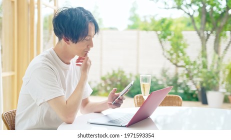 Young asian man using a laptop PC and a smart phone in casual room.