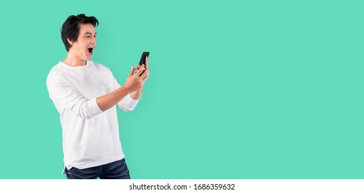Young Asian man using mobile phone with happy and cheerful over green background with copy space
