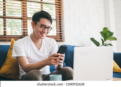 Young Asian Man Using Phone For Online Shopping, And Working With Laptop At Home