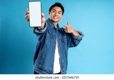 Young asian man using phone on a blue background - Shutterstock ID 2257646719