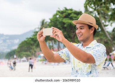 Young Asian Man Using Smartphone To Take Photo On The Tropical Beach.