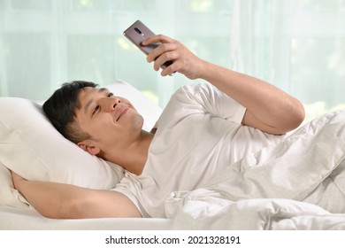 Young Asian man using smartphone in bed after waking up in the morning