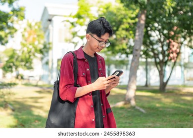 Young Asian man using smartphone with happy expression. A male smiling while holding his phone at the public park - Powered by Shutterstock