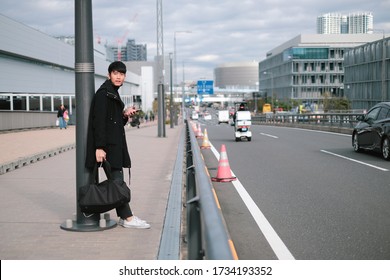 Young Asian Man Waiting For The Bus And Taxi In Big City. Fashion Model Photo Shoot