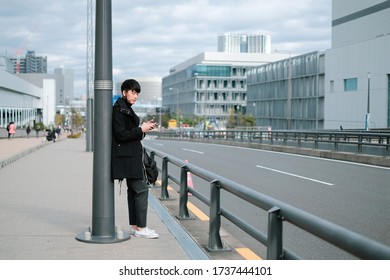 Young Asian Man Waiting For Bus And Taxi On Sidewalk