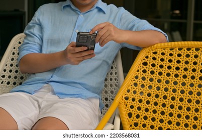 Young Asian Man Wear Casual Outfit Holds His Mobile Phone On His Hands, Searches For Some Informations In His Recreation Time, Holiday Trip.