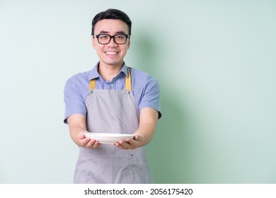 Young Asian man wearing apron posing on green background