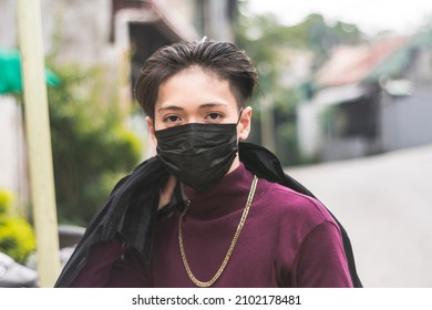 A Young Asian Man Wearing A Black Face Mask And In A Purple Sweater And A Big Gold Chain Necklace.