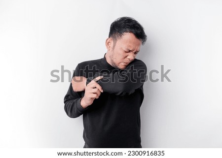 Young Asian man wearing black t-shirt standing over isolated white background smelling body odor, stinky and disgusting, intolerable smell. Bad smells concept.