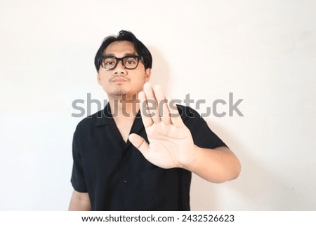 Young Asian man wearing black t-shirt on isolated white background doing stop sign with palm.