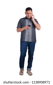 Young Asian Man Wearing Blue Jeans And Batik Shirt Shocked While Looking At His Phone. Isolated On White. Full  Body Portrait