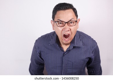 Young Asian man wearing blue shirt shouting because of anger. Against white wall
