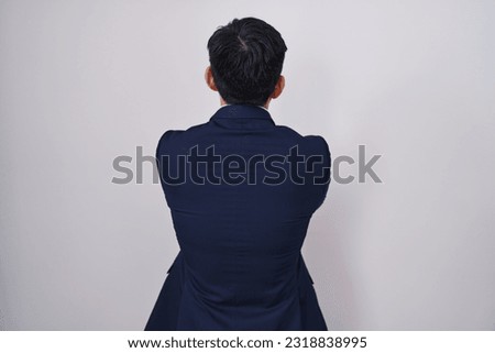 Young asian man wearing business suit and tie standing backwards looking away with crossed arms 