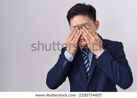 Young asian man wearing business suit and tie rubbing eyes for fatigue and headache, sleepy and tired expression. vision problem 