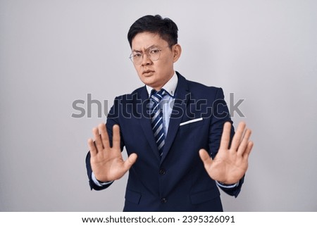 Young asian man wearing business suit and tie moving away hands palms showing refusal and denial with afraid and disgusting expression. stop and forbidden.  [[stock_photo]] © 