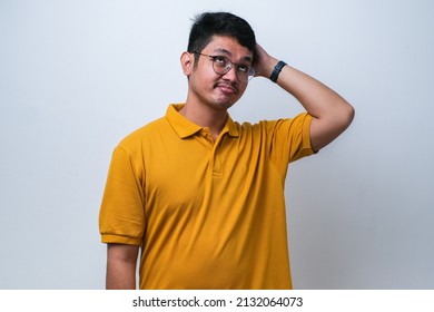 Young asian man wearing casual shirt standing over white background confuse and wonder about question. Uncertain with doubt, thinking with hand on head. Pensive concept.