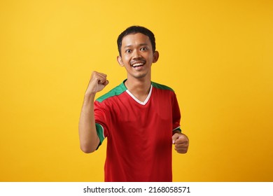 The Young Asian Man Wearing A Casual Sweater Standing On An Isolated Yellow Background Was Very Happy And Eager To Do A Win Gesture With His Arms Up, Shouting For Success. The Concept Of Celebration.