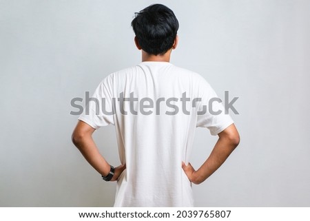 Young asian man wearing casual shirt over white background standing backwards looking away with arms on body