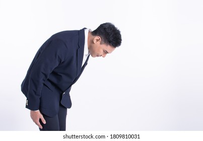 Young Asian Man Wearing Formal Suit And Bowing To Pay Respect Or Be Sorry While Standing On White Background With Copy Space. Business Manner Concept.