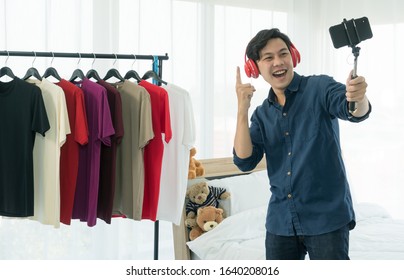 A Young Asian Man Wearing A Red Headset In His Ear Is Broadcasting Live Video Using A Mobile Phone Camera, Which Is An Online Product Review Through Social Media Such As YouTube And Facebook.