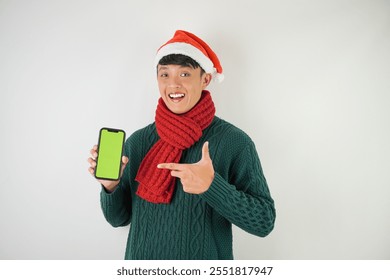 Young asian man wearing santa clause hat, red scarf and green long sleeved sweater is showing smartphone green screen, isolated over white background. - Powered by Shutterstock