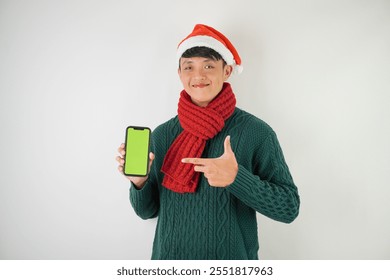 Young asian man wearing santa clause hat, red scarf and green long sleeved sweater is showing smartphone green screen, isolated over white background. - Powered by Shutterstock