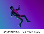 Young Asian man wearing VR headset enjoy playing video game and levitating in the air on futuristic purple cyberpunk neon light banner background. Metaverse technology concept.