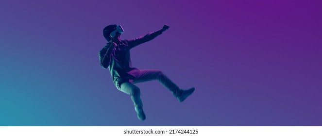 Young Asian man wearing VR headset playing video game and levitating in the air on futuristic purple cyberpunk neon light banner background. Metaverse technology concept. - Shutterstock ID 2174244125