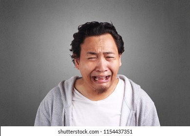 Young Asian man wearing white shirt and gray jacket crying expression. Background on gray. Close up head and shoulders