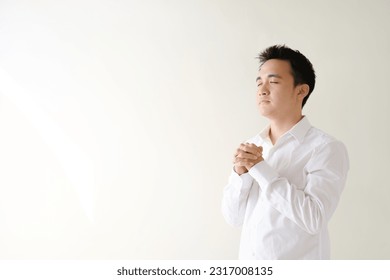 Young Asian man wearing a white shirt praying and facing to his right angled - Powered by Shutterstock