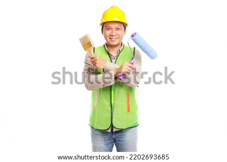 young asian man wearing yellow hard hat and work safety clothing holding paint roller brush isolated on white background