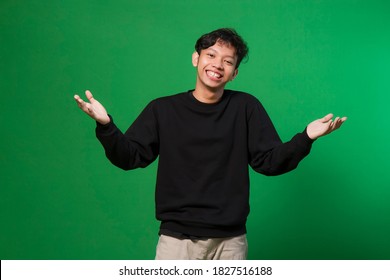 Young Asian Man Welcoming Everyone With His Arms Wide Open And A Big Smile. Emotions, Facial Expressions, Feelings, Body Language, Signs. Isolated On Green Background.