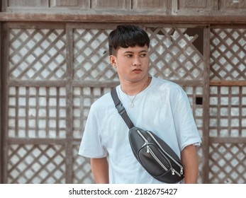 A Young Asian Man In A White Shirt With A Black Sling Bag In Front Of An Old House.