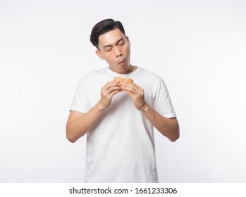 Young Asian Man In White T-shirt Eating Hamburger With Happy Face Isolated Over White Background.