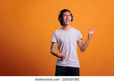 Young asian man in wireless, headphones playing virtual guitar, rockstar lifestyle. Teenage guitarist practicing, using imaginable musical instrument, fun pastime, leisure activity