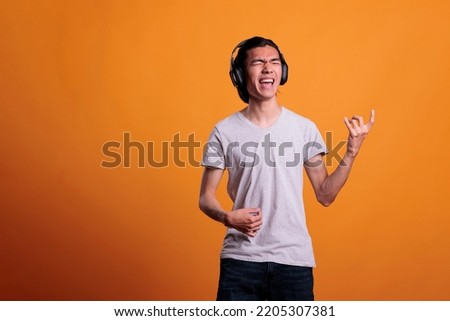 Young asian man in wireless, headphones playing virtual guitar, rockstar lifestyle. Teenage guitarist practicing, using imaginable musical instrument, fun pastime, leisure activity