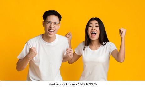 Young asian man and woman celebrating success over yellow background, clenching fists and shouting, panorama