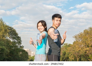 Young Asian Man And Woman Drinking Water From A Bottle And Thumbs-up